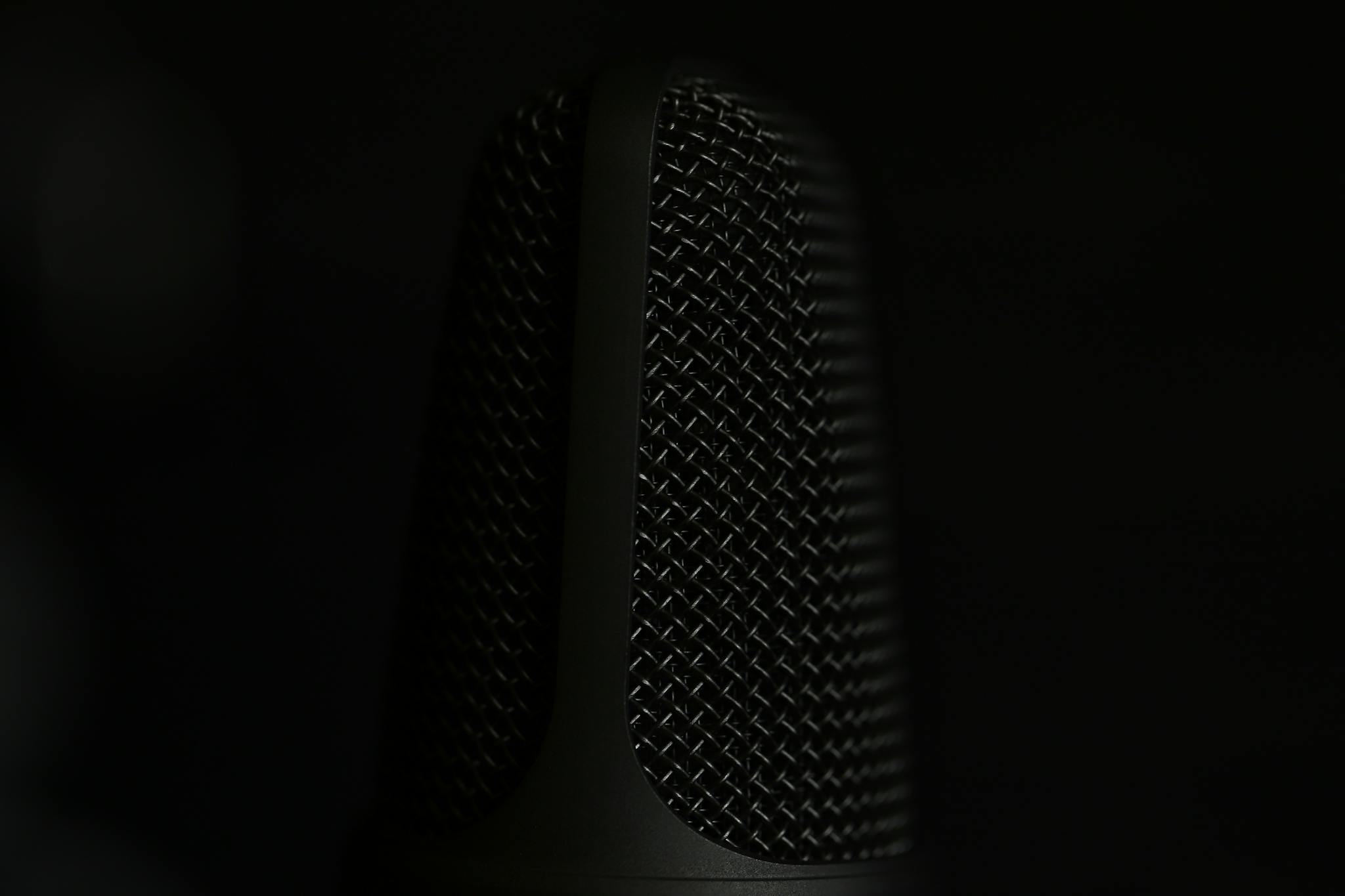 A detailed macro shot of a microphone in a studio setting with a dark background.