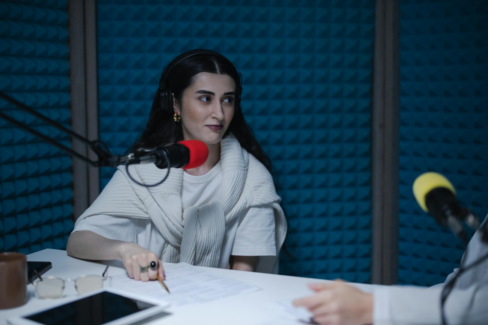 A woman in a podcast studio with microphones and headphones, focused on a discussion.